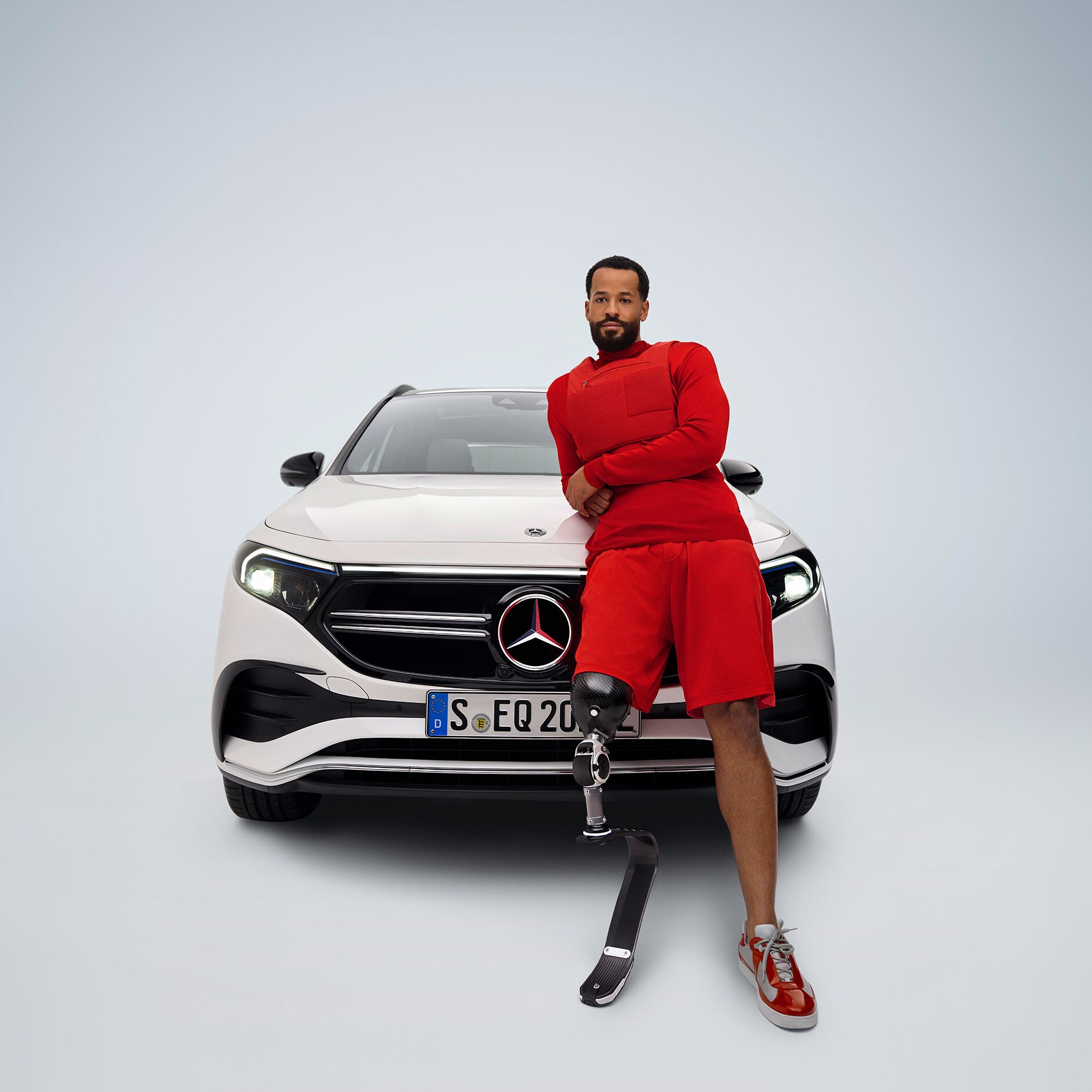 Pedalanpassungen | Fahrhilfen | Mercedes-Benz Der behindertengerecht umgebaute Mercedes-Benz EQA in einer Frontansicht und ein Mann mit Beinprothese.