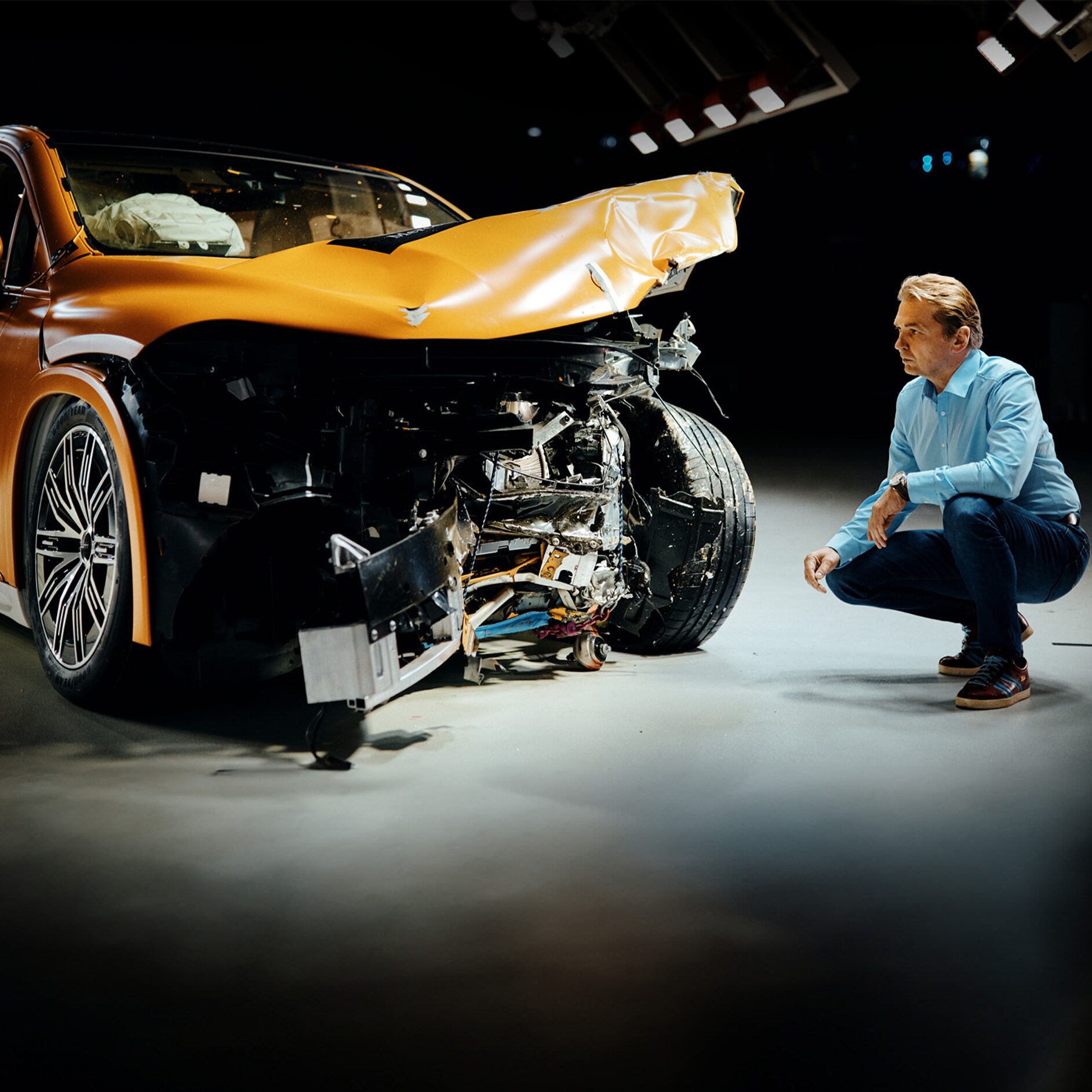 Esperti di crash test | Sicurezza | Mercedes-Benz Un esperto di crash test mentre esamina una Mercedes-Benz incidentata anteriormente accovacciato sul letto.