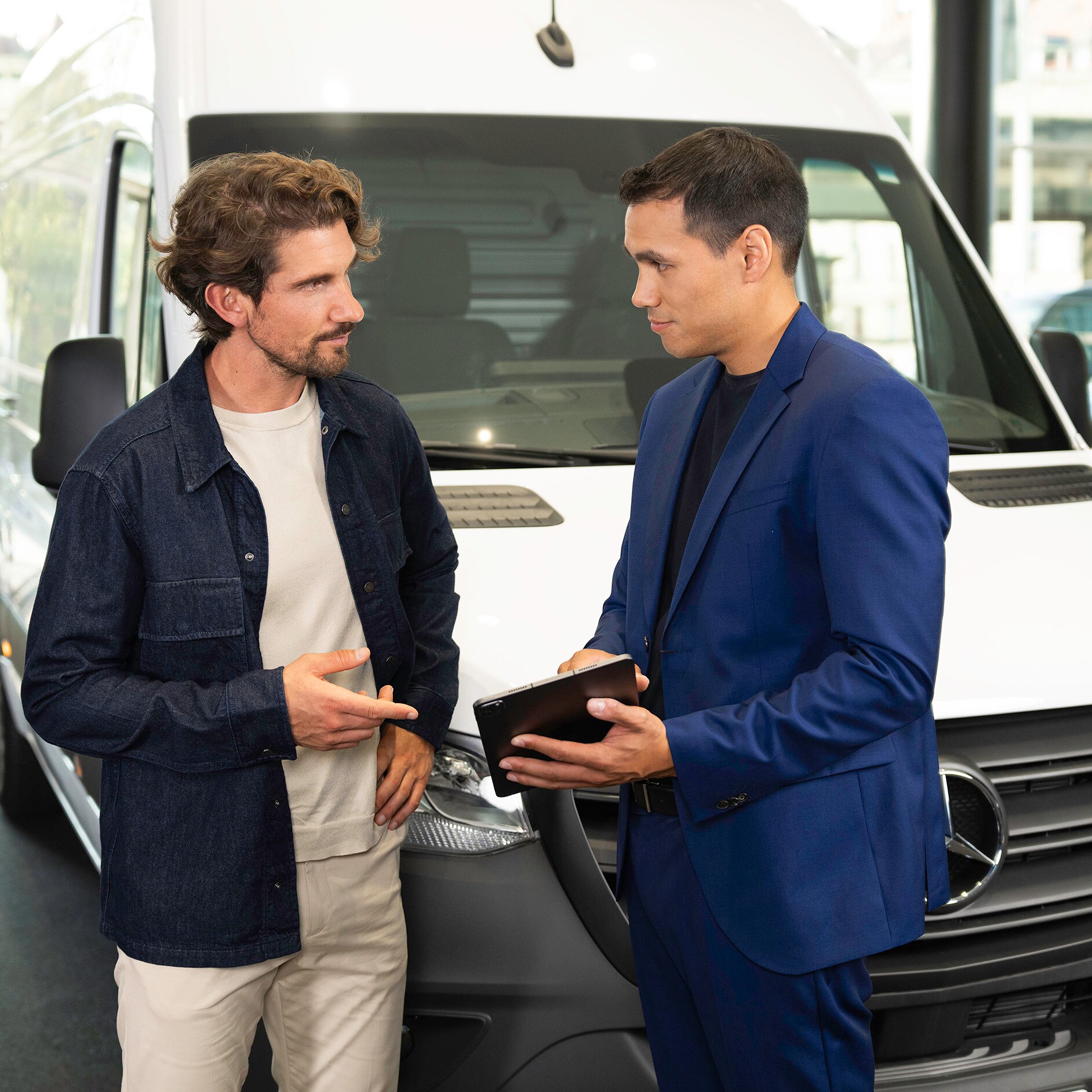 Un leasing pour votre Mercedes-Benz Deux personnes qui parlent et pointent du doigt un appareil mobile tout en se tenant devant un van Mercedes-Benz.
